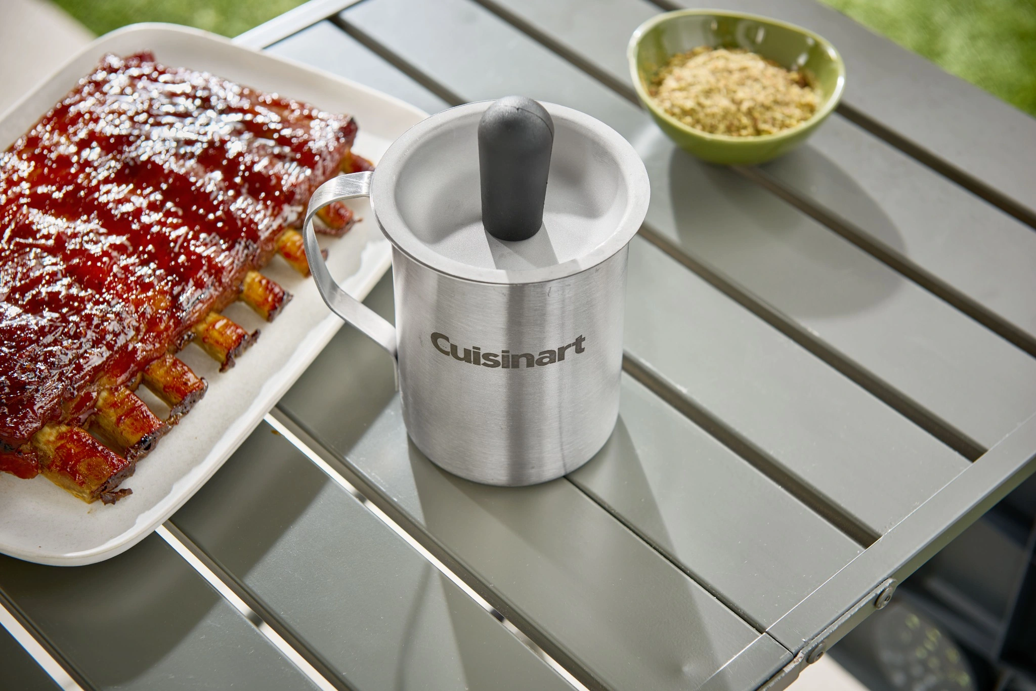 Cuisinart basting brush and stainless steel pot beside ribs on an outdoor table