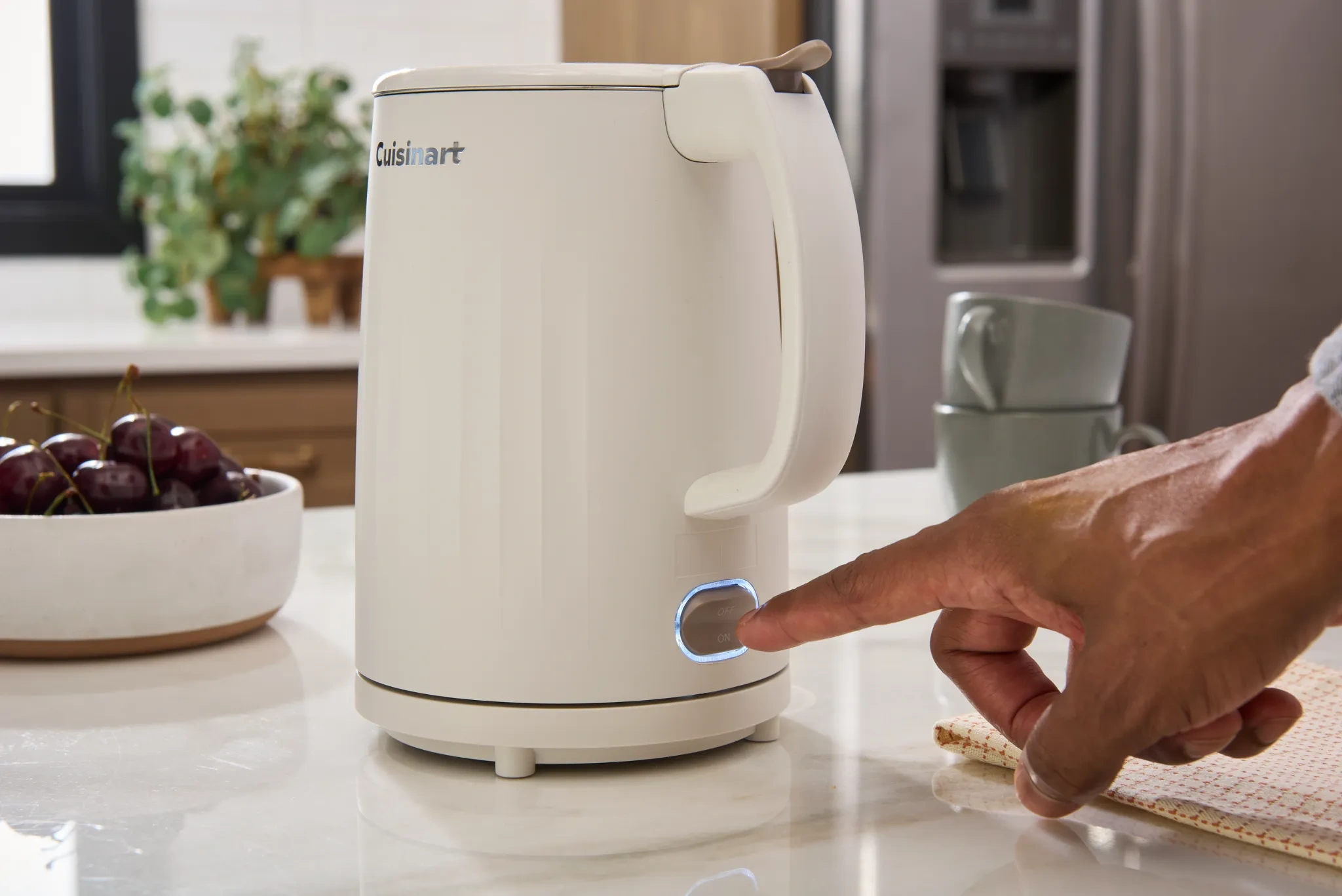 A hand switches on a Cuisinart kettle in a warmly styled kitchen